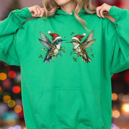 May include: A bright green hooded sweatshirt featuring a graphic of two hummingbirds wearing red and white Santa hats. The birds are decorated with colorful Christmas light strings and green holly leaves, centered on the front of the garment.
