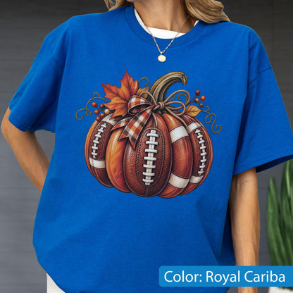 May include: A royal blue short-sleeve t-shirt featuring a graphic of a pumpkin designed with the texture and white laces of an American football. The pumpkin is decorated with a plaid ribbon, autumn leaves, and small red berries on its stem.