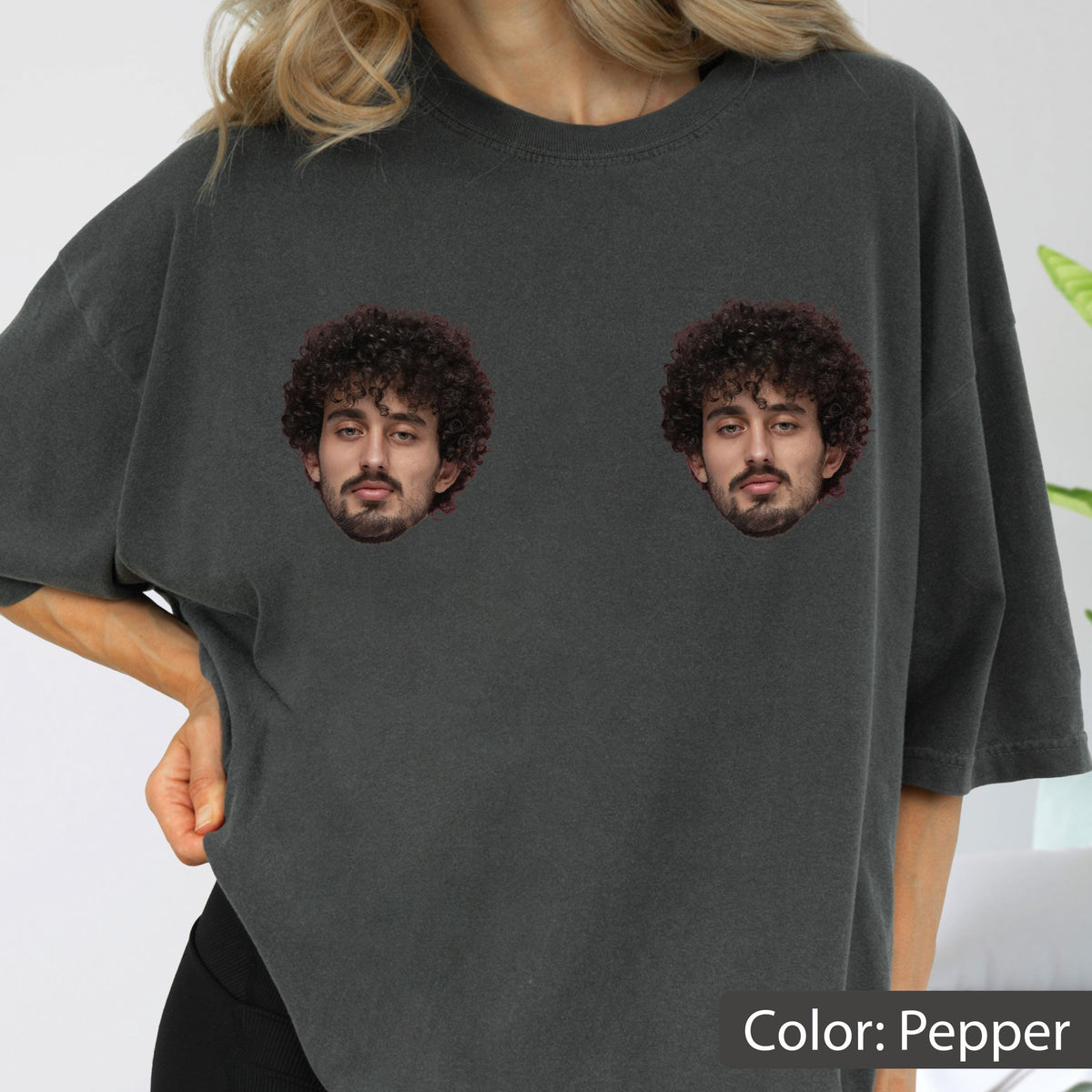 May include: A charcoal gray short-sleeved t-shirt featuring two identical photographic prints of a person with dark curly hair and a beard positioned on the chest area. The shirt has a relaxed fit and a solid, muted dark gray color throughout.