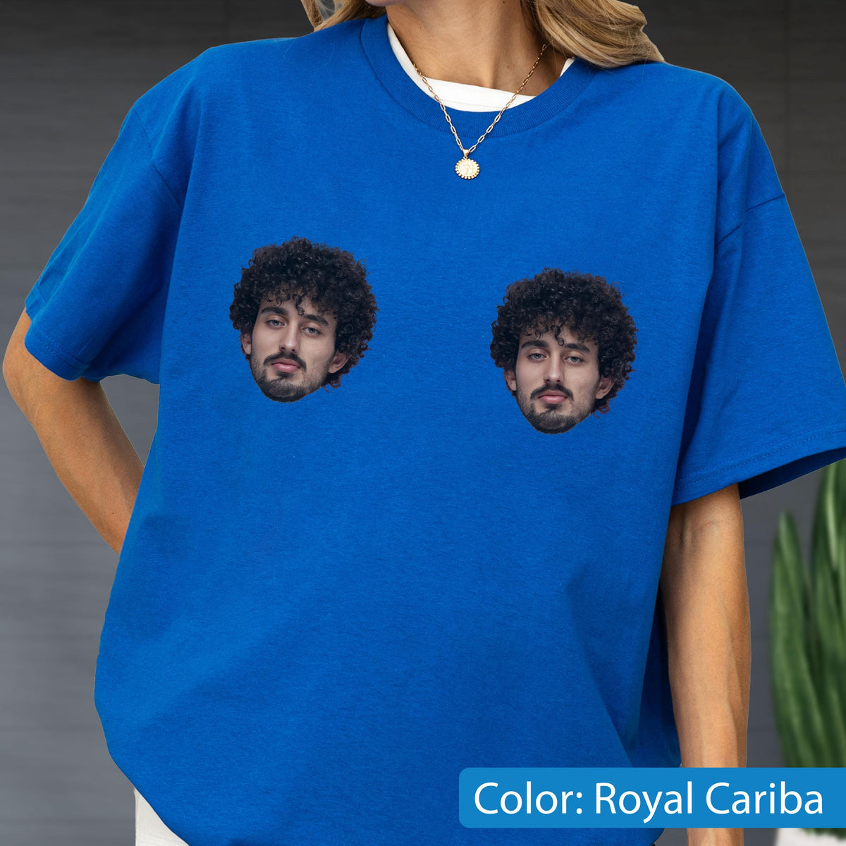 May include: A royal blue short-sleeved t-shirt featuring two identical photographic prints of a person with dark curly hair and a beard. The shirt has a crew neckline and is made of a solid-colored fabric. The graphic is centered on the chest.