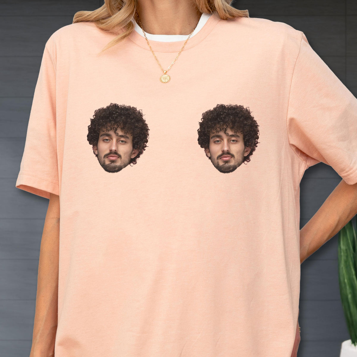 May include: A peach-colored short-sleeve t-shirt featuring two identical photographic prints of a person with dark curly hair and a beard positioned on the chest area. The shirt has a crew neckline and a relaxed fit, showcasing a custom graphic design.