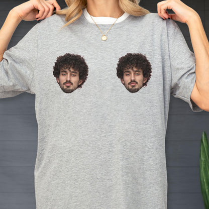 May include: A heather gray short-sleeve t-shirt featuring two identical photographic prints of a person with dark curly hair and a beard, positioned side-by-side on the chest area of the garment. The shirt has a crew neckline.