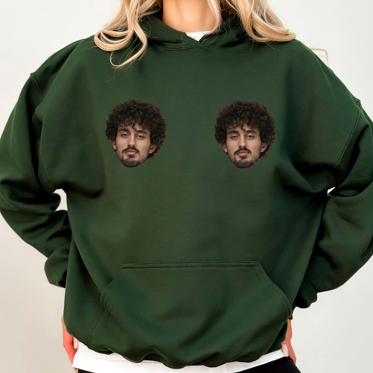 May include: A dark forest green hooded sweatshirt featuring a large front kangaroo pocket and two identical photographic prints of a person with dark curly hair and a beard positioned on the upper chest area of the garment.