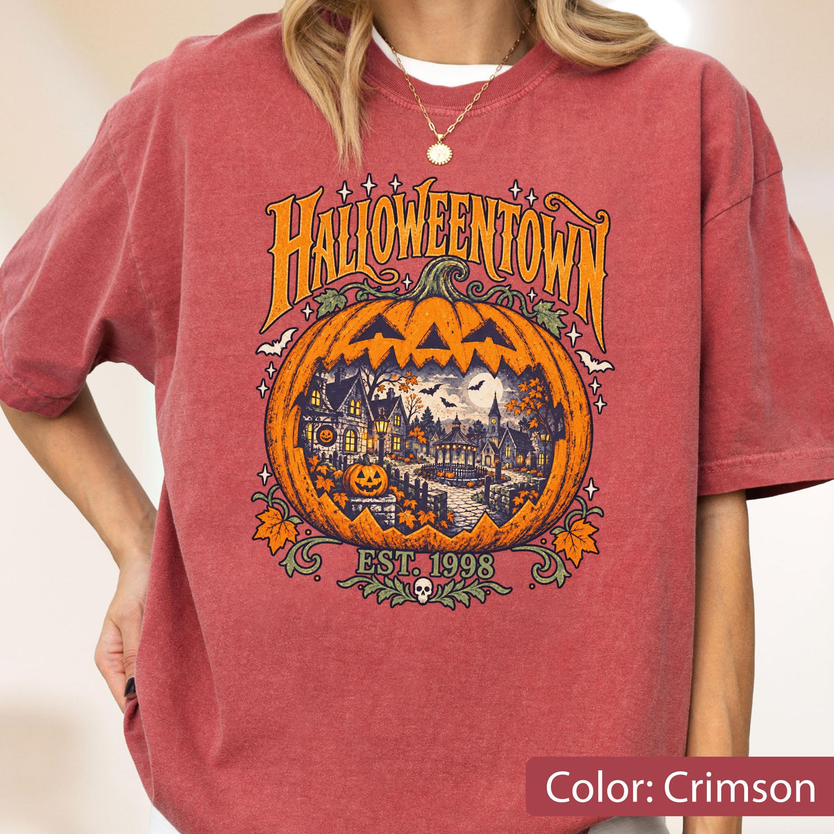 May include: A crimson short-sleeve t-shirt featuring a large graphic of a jack-o'-lantern containing a spooky town scene. The text reads HALLOWEENTOWN and EST. 1998. The design includes bats, autumn leaves, and a small skull at the bottom center.