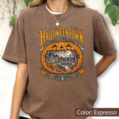 May include: An espresso brown t-shirt featuring a large graphic of a carved pumpkin with a spooky town scene inside. The text reads HALLOWEENTOWN and EST. 1998. The design includes orange, yellow, and dark blue colors with small stars and leaves.