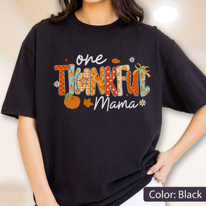 May include: Black t-shirt with the words "one THANKFUL Mama" in a colorful, fall-themed design. The text features pumpkins, leaves, and floral accents. The shirt is a comfortable, casual style.