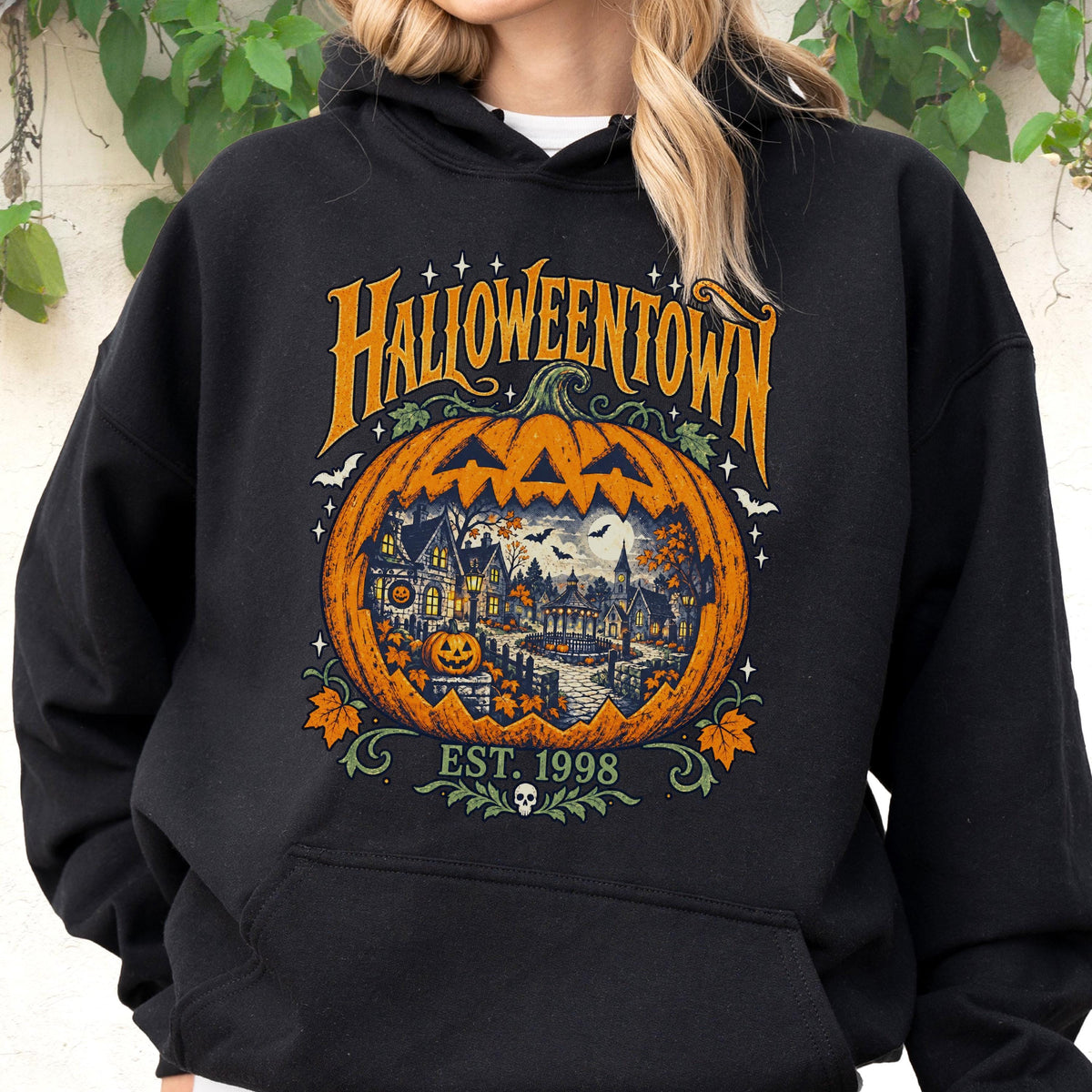 May include: A black hooded sweatshirt featuring a large graphic of a carved pumpkin with a detailed scene of a spooky town inside. The text HALLOWEENTOWN is printed in orange above the pumpkin, with EST. 1998 and a small skull icon below it.