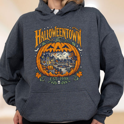 May include: A dark heather gray hooded sweatshirt featuring a large graphic print of a carved pumpkin. Inside the pumpkin is a detailed scene of a town with houses and trees. The text reads HALLOWEENTOWN and EST. 1998 with a small skull icon.