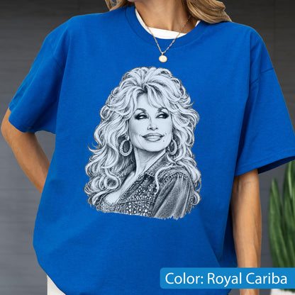 May include: A royal blue short-sleeved t-shirt featuring a detailed black and white sketch-style graphic of a person with voluminous hair, hoop earrings, and a textured jacket. The shirt has a crew neckline and a relaxed, boxy fit.