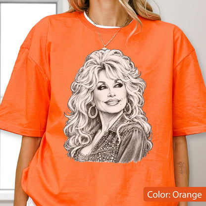 May include: A bright orange short-sleeved t-shirt featuring a detailed black and white pencil-style sketch of a woman with voluminous blonde hair, hoop earrings, and a denim jacket. The graphic is centered on the chest of the garment.