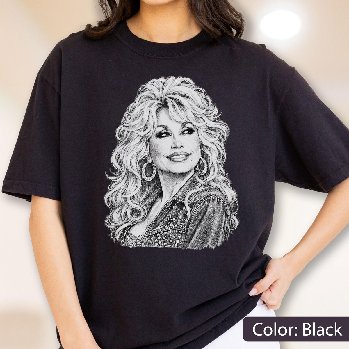 May include: A black short-sleeved t-shirt featuring a detailed white line-art illustration of a person with voluminous wavy hair, wearing large hoop earrings and a textured jacket. The graphic is centered on the chest of the garment.