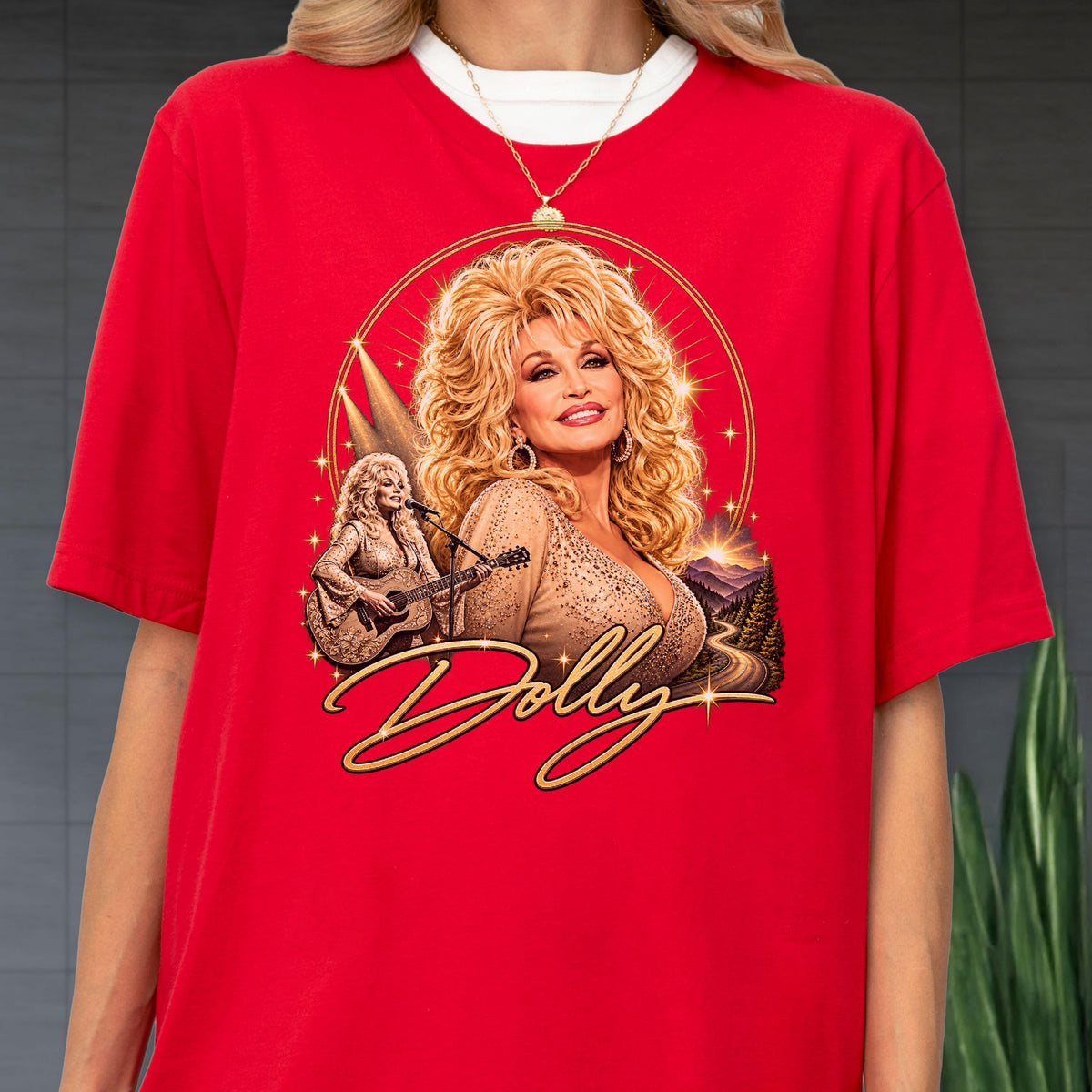 May include: A bright red short-sleeved t-shirt featuring a graphic print of Dolly Parton with voluminous blonde hair. The design includes a smaller image of her playing an acoustic guitar, golden starburst accents, and the name Dolly in script.