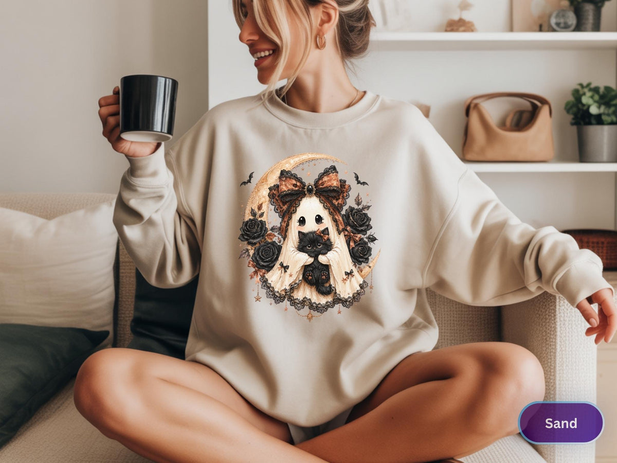 May include: A sand-colored crewneck sweatshirt featuring a graphic print of a ghost wearing a large patterned bow, holding a black cat, surrounded by black roses, small bats, and a crescent moon. The sweatshirt has long sleeves and a ribbed collar.