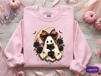 May include: A light pink crewneck sweatshirt featuring a graphic print of a ghost wearing a large leopard print bow and holding a black kitten. The design includes a crescent moon, black roses, small bats, and hanging star charms.