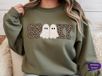 May include: A military green crewneck sweatshirt featuring the text SPOOKY in a varsity-style font. The letters S, P, K, and Y have a brown and black leopard print pattern, while the two O's are replaced by white lace-textured ghost figures.