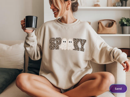 May include: A sand-colored crewneck sweatshirt featuring the word SPOOKY printed across the chest. The letters S, P, O, K, and Y are filled with a brown and black leopard print pattern, while the two O's are replaced by white ghost illustrations.