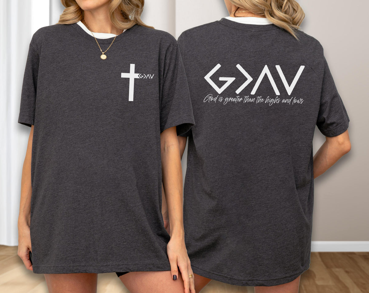 May include: Dark gray t-shirt with a white cross and the text ">AV" on the front. The back of the shirt features the text "G>AV" above the phrase "God is greater than the highs and lows" in white.