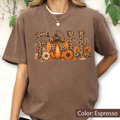 May include: An espresso-colored short-sleeve t-shirt featuring the word FALL in a leopard print pattern. The letter A is replaced by an orange pumpkin with a leopard print bow, surrounded by sunflowers and autumn leaves at the base of the text.