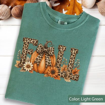 May include: A light green crewneck t-shirt featuring the word FALL in a leopard print pattern. The letter A is replaced by an orange pumpkin with a leopard print bow. The design includes sunflowers and autumn leaves surrounding the text.