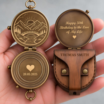 A hand holding a personalized compass with a wooden case and a message engraved on it.