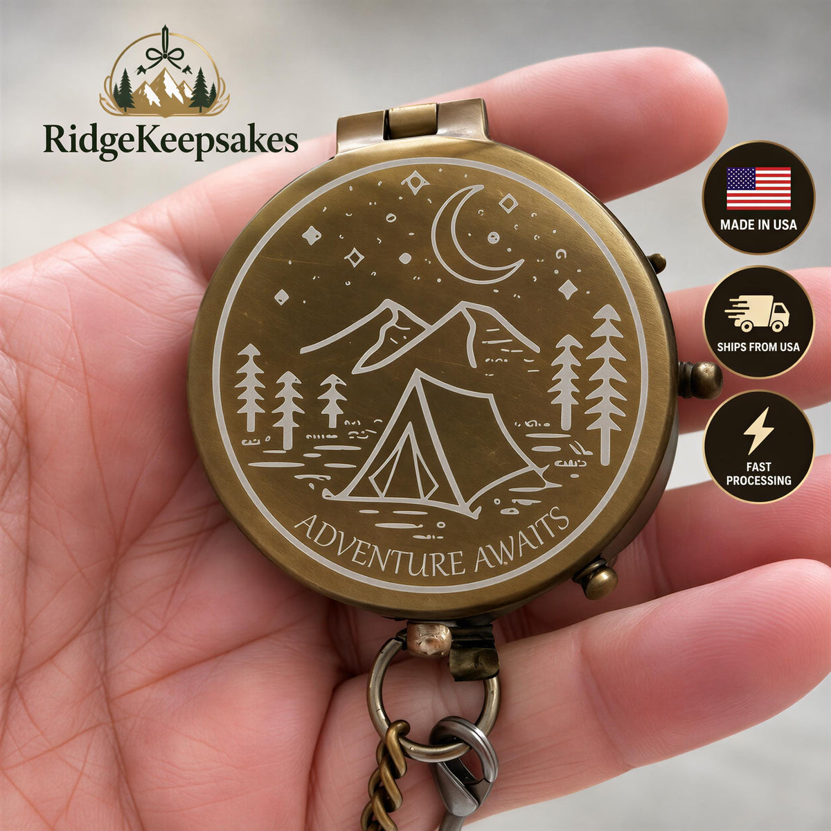 A hand holding a compass with a design of a mountain landscape and camping scene, along with the text "Adventure Awaits".