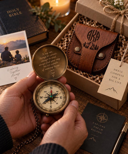 A person's hands holding a compass with a personalized message engraved on it, surrounded by other items such as a Bible, a leather wallet, and a note.