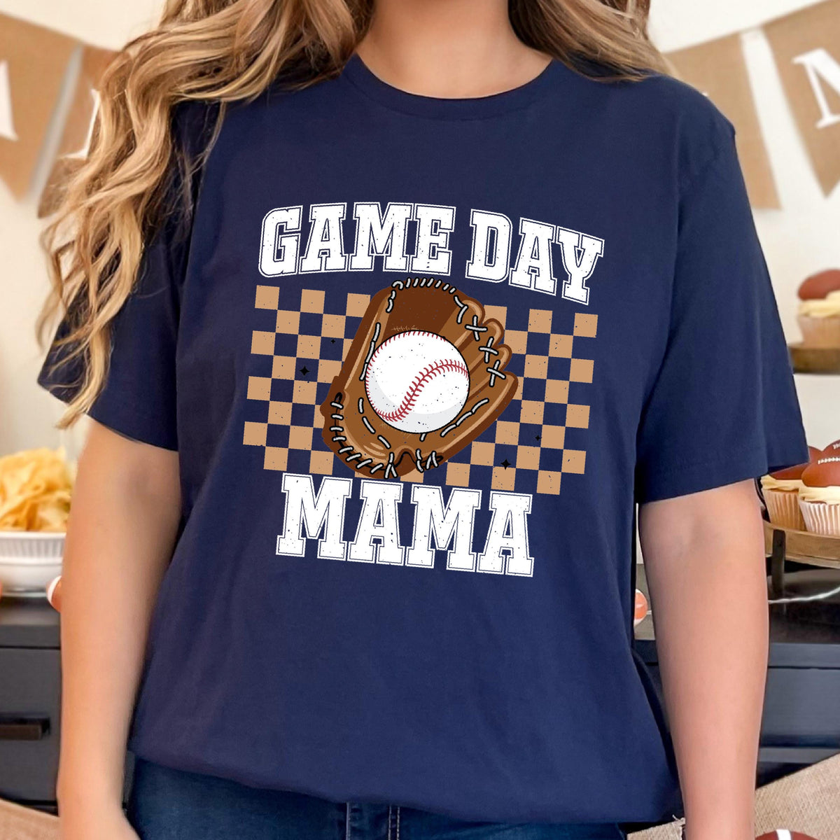 May include: Navy blue t-shirt with the words "GAME DAY MAMA" in white block letters. A baseball glove and baseball are in the center of the shirt, set against a brown and tan checkered background.