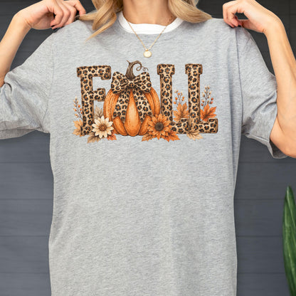 May include: A heather gray t-shirt featuring the word FALL in a leopard print pattern. The letter A is replaced by an orange pumpkin with a leopard print bow. The design includes sunflowers and autumn leaves surrounding the base of the letters.