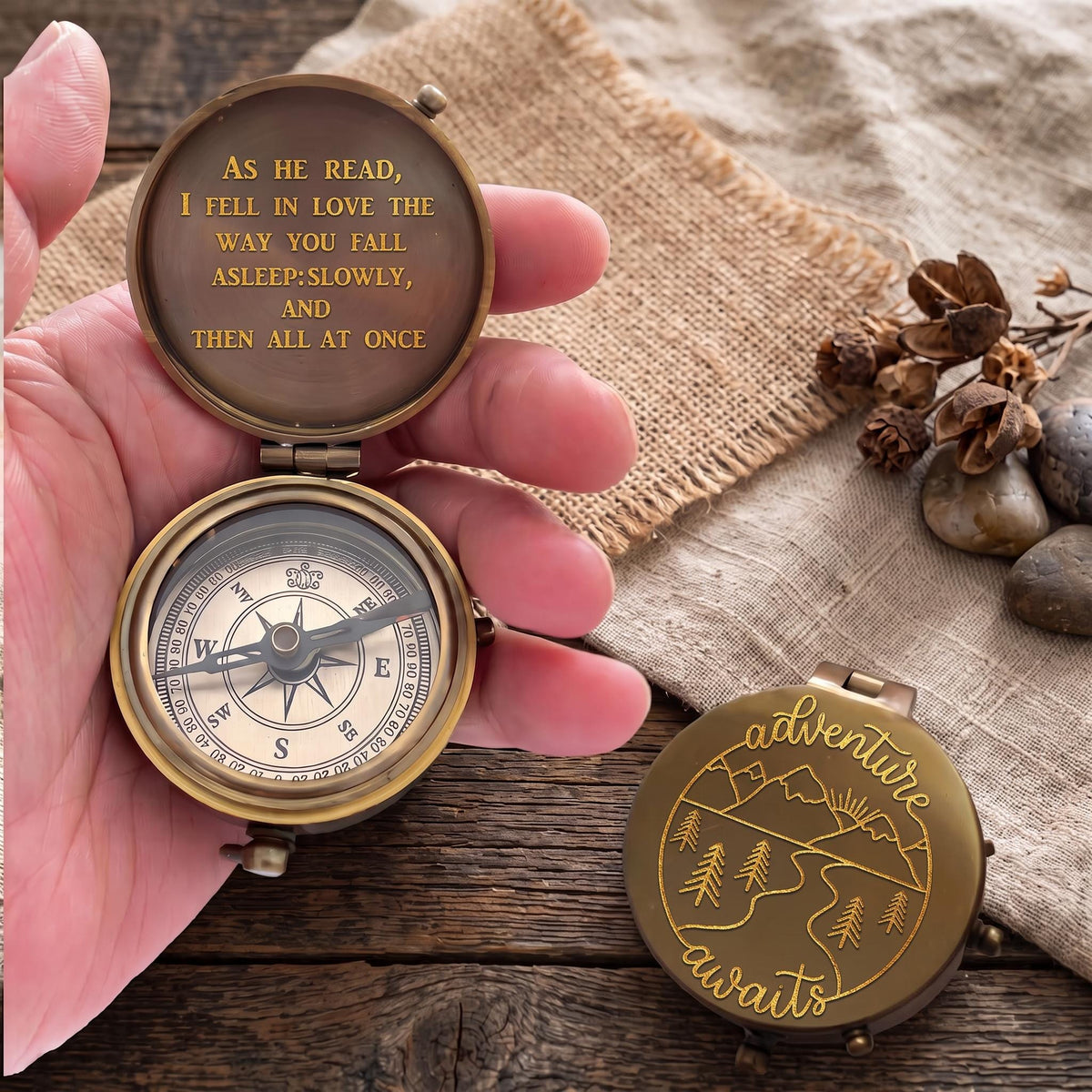 May include: A round brass pocket compass with a hinged lid. The interior lid features the engraved text: As he read, I fell in love the way you fall asleep: slowly, and then all at once. The exterior lid displays an engraved mountain landscape.