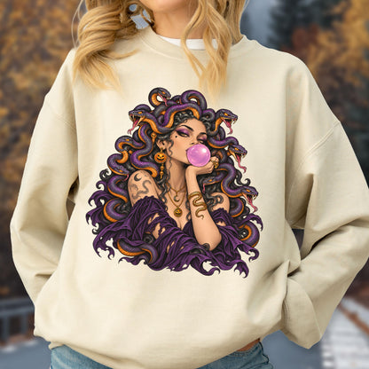 May include: A beige crewneck sweatshirt featuring a graphic print of a figure with purple snakes for hair, wearing a dark purple off-the-shoulder top, gold jewelry, and blowing a pink bubble with gum. The design includes intricate snake details.