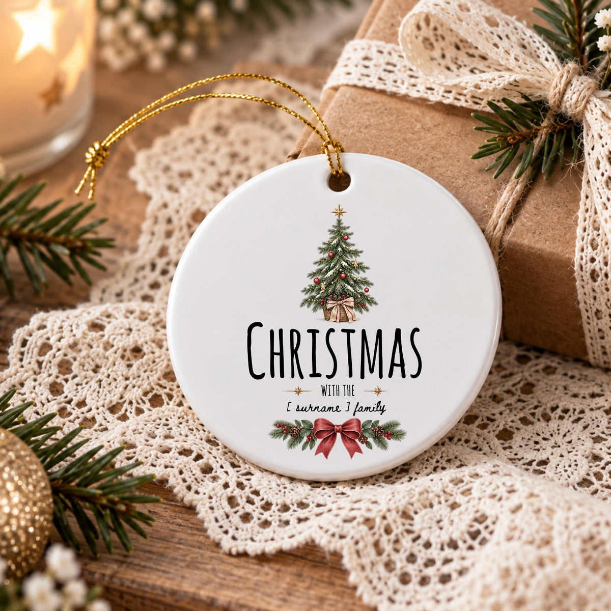 May include: A round white ceramic ornament featuring a printed illustration of a decorated Christmas tree, a red bow, and pine branches. The text reads CHRISTMAS WITH THE [ surname ] family in black lettering, suspended by a gold string.