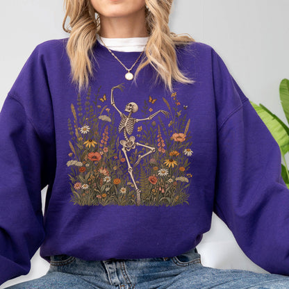 May include: A deep purple long-sleeve sweatshirt featuring a graphic print of a skeleton dancing amidst a field of colorful wildflowers, including daisies, poppies, and tall grasses, with small butterflies scattered throughout the floral scene.