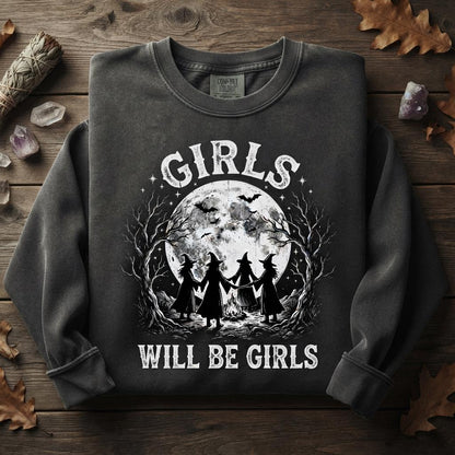 May include: A charcoal gray crewneck sweatshirt featuring a white graphic print of four figures in witch hats holding hands around a campfire. Above the scene is a large full moon with bats, and the text reads GIRLS WILL BE GIRLS in white.