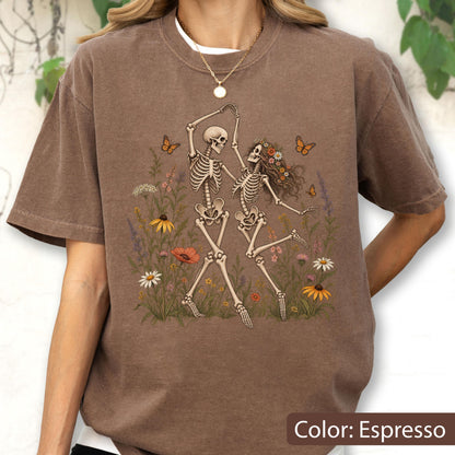 May include: An espresso-colored t-shirt featuring a graphic print of two skeletons dancing amidst a field of colorful wildflowers and orange butterflies. The design includes various floral elements in shades of yellow, red, and white.