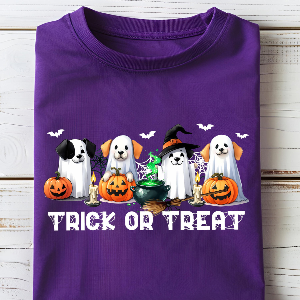 May include: A purple t-shirt featuring a Halloween design. The graphic includes four dogs dressed as ghosts, pumpkins, candles, bats, a witch's cauldron, and the text "TRICK OR TREAT" in white.