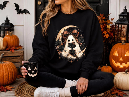 May include: A black long-sleeve sweatshirt featuring a graphic print of a white ghost wearing a large orange and black patterned bow, holding a small black kitten, surrounded by black roses and a crescent moon against a dark background.