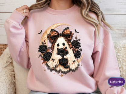 May include: A light pink crewneck sweatshirt featuring a graphic print of a ghost wearing a large patterned bow and holding a black kitten. The design includes a crescent moon, black roses, and small bats, all rendered in a detailed illustration.