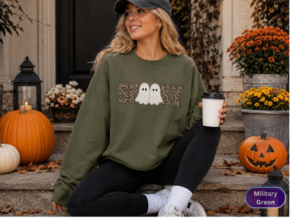 May include: A military green long-sleeve sweatshirt featuring the word SPOOKY in a leopard print pattern with two white ghost illustrations replacing the letter O. The garment has a crew neckline and long sleeves, providing a casual fit.