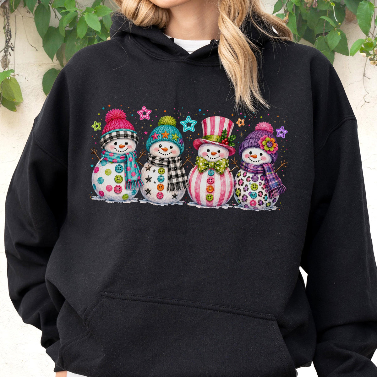 May include: A black hooded sweatshirt featuring a graphic print of four snowmen standing in a row. Each snowman wears a colorful hat and scarf, with buttons on their bodies and small star shapes scattered in the background above them.