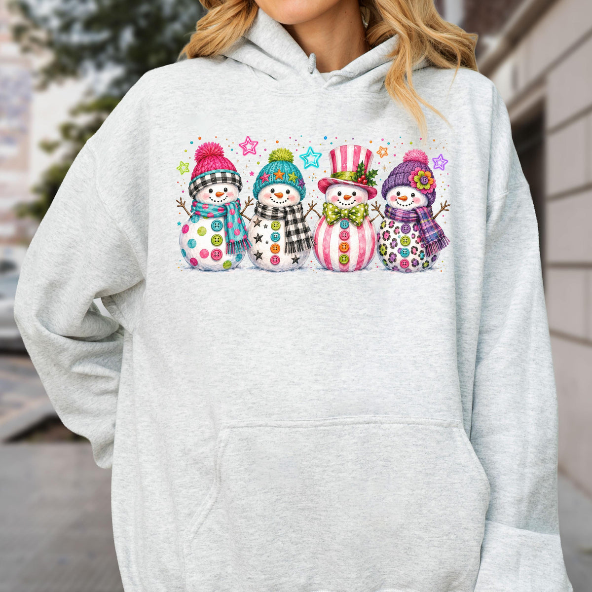 May include: A light gray hooded sweatshirt featuring a graphic print of four snowmen standing in a row. Each snowman wears a colorful winter hat and scarf, decorated with various patterns, buttons, and small stars in the background.