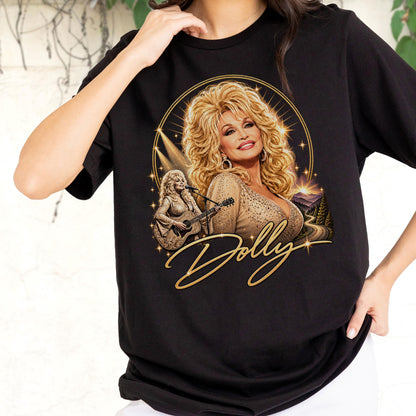 May include: A black t-shirt featuring a graphic print of Dolly Parton with blonde hair, wearing a gold embellished top. The design includes a smaller image of her playing an acoustic guitar, a mountain landscape, and the word Dolly in gold script.