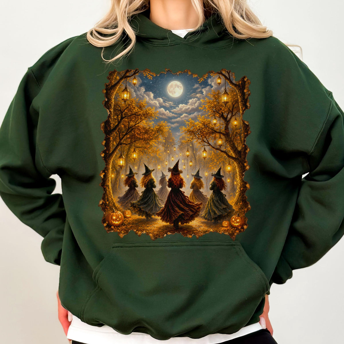 May include: A dark forest green hooded sweatshirt featuring a rectangular graphic print of five figures wearing pointed hats and long dresses standing in a moonlit autumn forest with hanging lanterns, golden trees, and orange pumpkins on the ground.