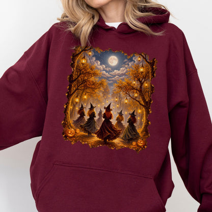 May include: A maroon hooded sweatshirt featuring a rectangular graphic print of several figures in pointed hats dancing in a forest at night. The scene includes glowing lanterns hanging from autumn trees, a full moon in the sky, and orange pumpkins.
