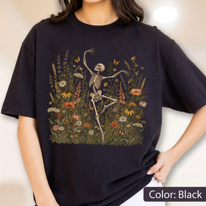 May include: A black t-shirt featuring a graphic print of a skeleton dancing amidst a field of colorful wildflowers and small butterflies. The illustration includes various botanical elements in shades of orange, yellow, white, and green.