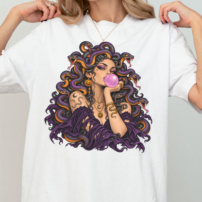 May include: A white t-shirt featuring a graphic illustration of a figure with purple snakes for hair, wearing a dark purple off-the-shoulder top, blowing a pink bubblegum bubble, and adorned with gold jewelry including pumpkin-shaped earrings.