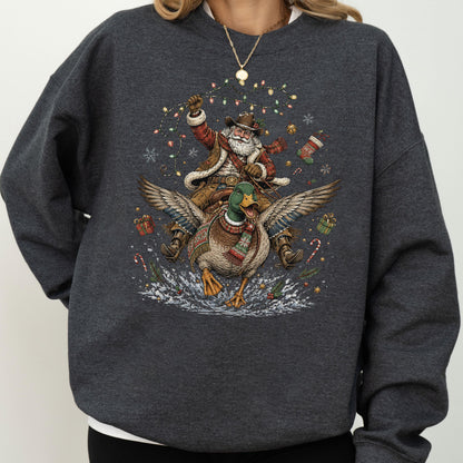 May include: A dark charcoal gray crewneck sweatshirt featuring a graphic print of Santa Claus wearing a cowboy hat and vest, riding a flying mallard duck. The design includes colorful Christmas lights, snowflakes, gift boxes, and candy canes.