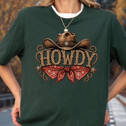 May include: A dark green t-shirt featuring a graphic print of a brown cowboy hat above the word HOWDY written in a rope-style font. Below the text is a red bandana with a white floral pattern and two small silver-toned star accents.