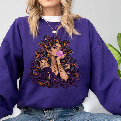 May include: A deep purple crewneck sweatshirt featuring a graphic illustration of a figure with snakes for hair, blowing a pink bubblegum bubble. The figure wears a dark purple off-the-shoulder top and gold jewelry, set against a solid purple background.