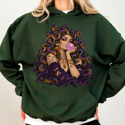 May include: A dark forest green hooded sweatshirt featuring a graphic illustration of a figure with snakes for hair, blowing a pink bubble. The figure wears layered necklaces and a dark purple garment, surrounded by purple and orange snakes.