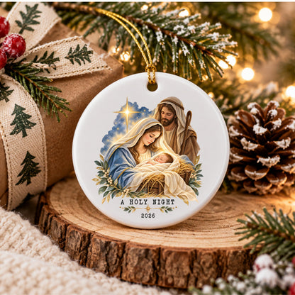May include: A round white ceramic Christmas ornament featuring a colorful illustration of the Nativity scene with Mary, Joseph, and the baby Jesus. The text A HOLY NIGHT and the year 2026 are printed in black at the bottom of the ornament.